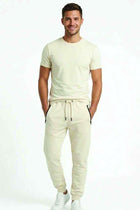 Men's off-white jogger trousers with drawstring waist, zip pockets, and tapered fit