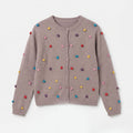 GirlsÃ¢â‚¬â„¢ grey knit cardigan with button front and colorful pom-pom accents.